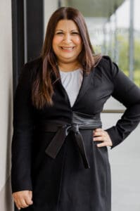 Dr Samia in a black blazer smiling outdoors.