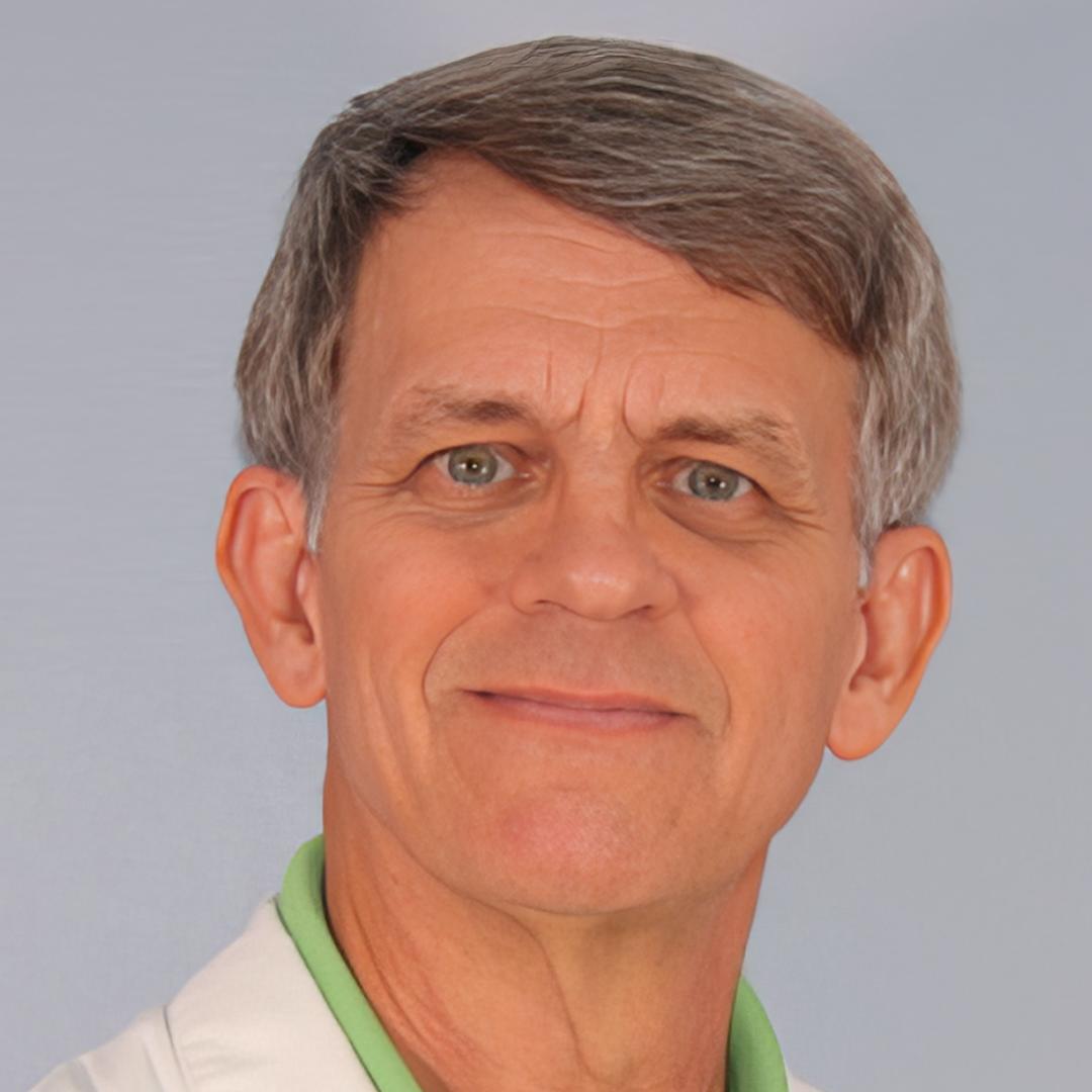 A close-up portrait of an older man with short gray hair, wearing a white collared shirt and smiling softly.