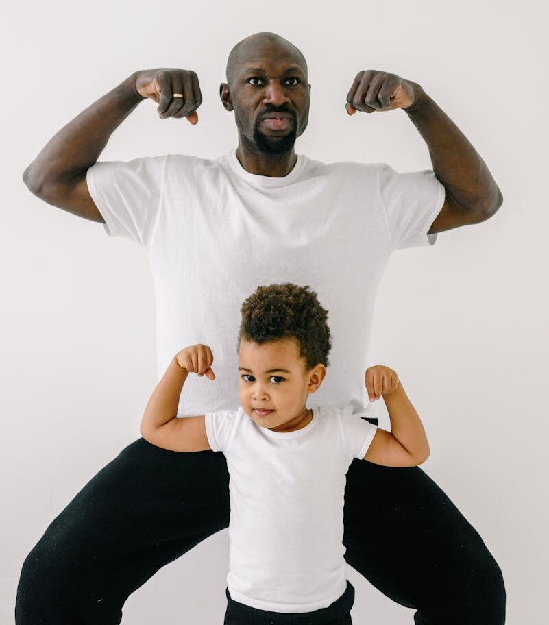 African American father and son flexing muscles against white backdrop